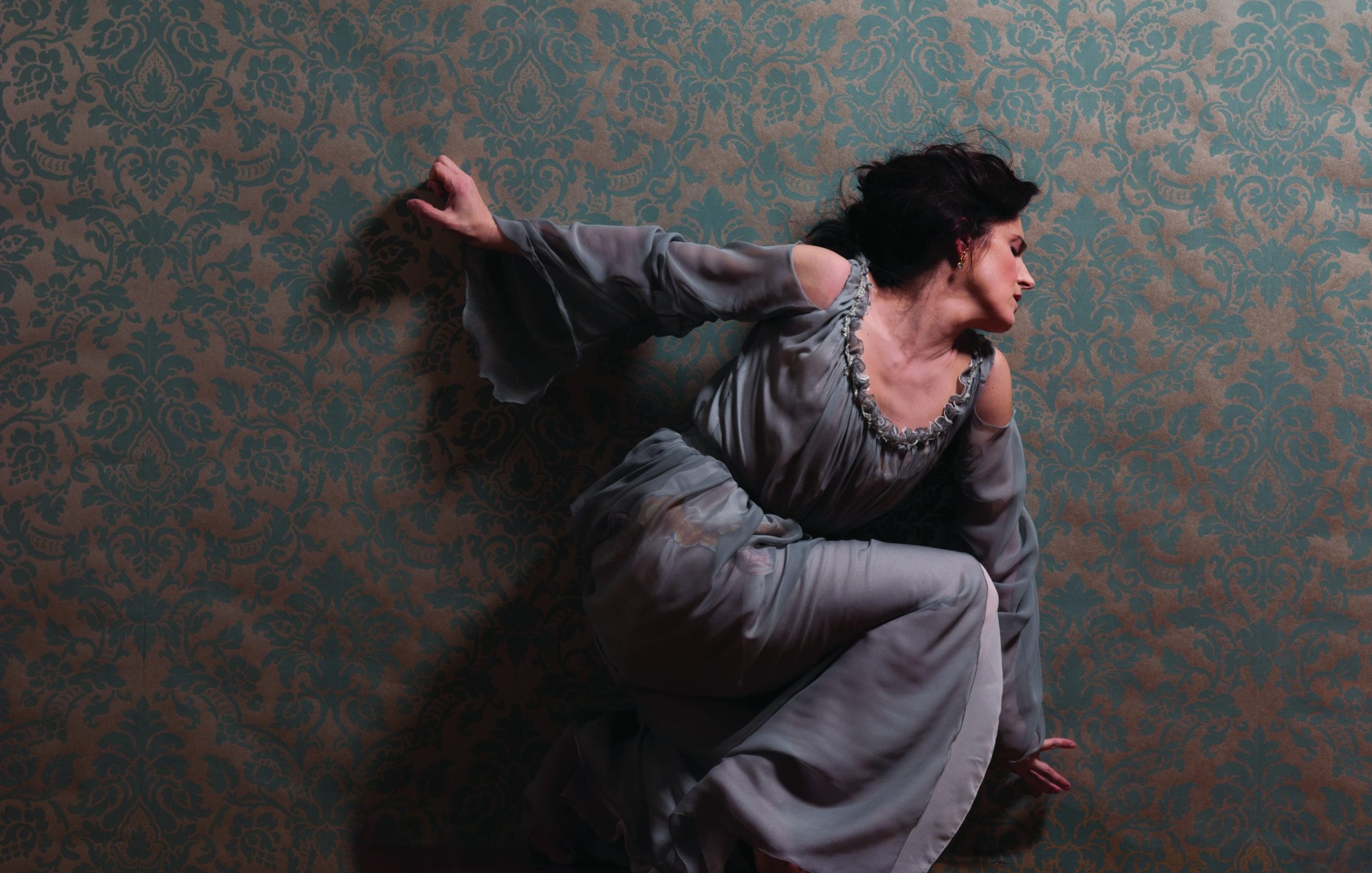 Dancer Laurence Lemieux kneeling in front of turquoise wallpaper